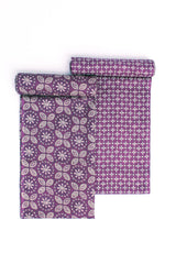 A rolled-up fabric with orange, green, and cream geometric patterns on a purple base, along with stylized floral designs.