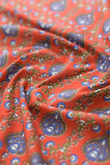Close-up of red fabric with blue and green paisley patterns.