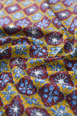 Close-up of patterned fabric with blue and red designs on a yellow background.