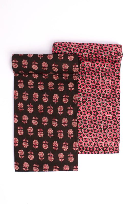 Two pieces of fabric, one with a blush pink floral pattern on a charcoal background and the other with a geometric pattern in the same color scheme.