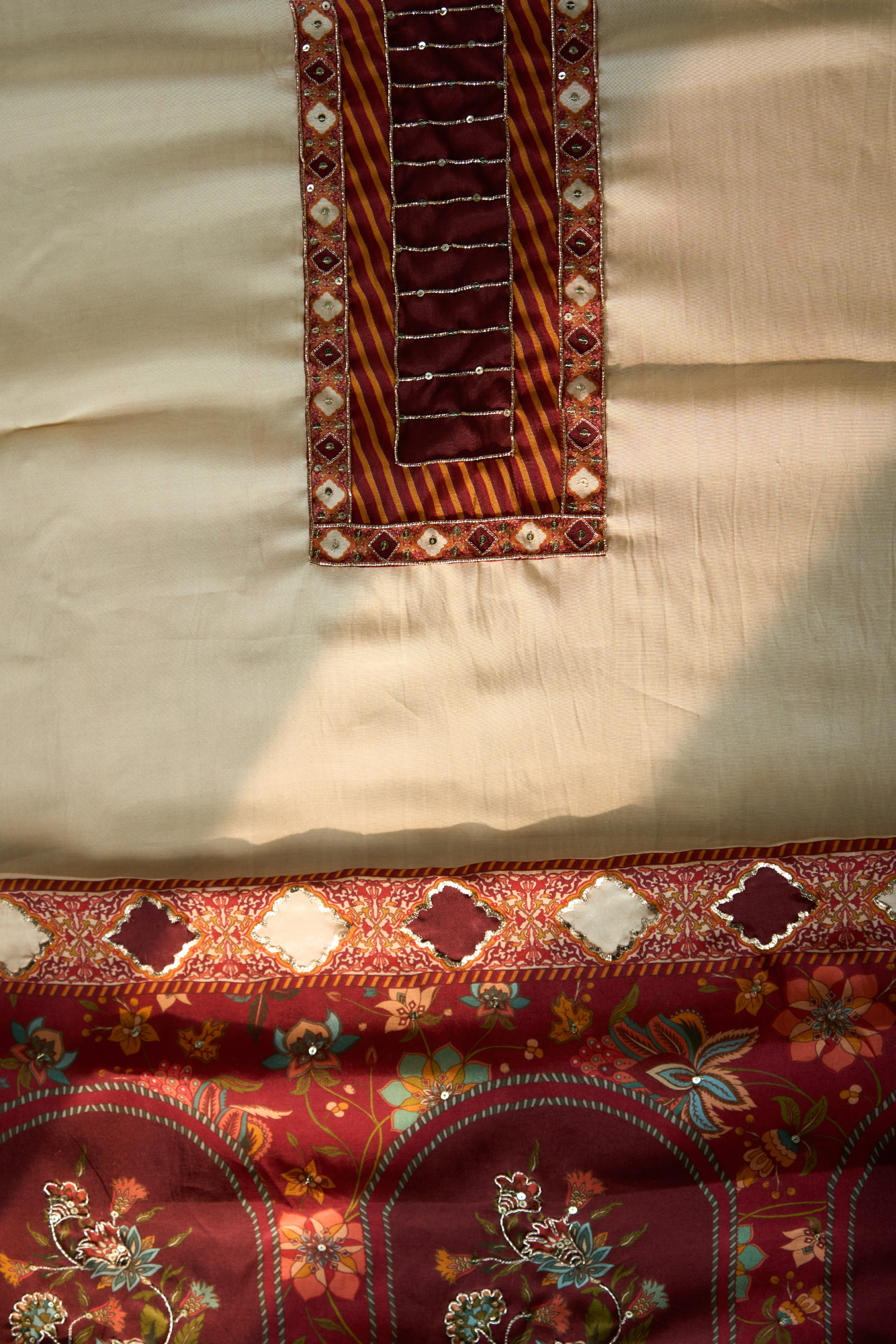 Close-up of embroidered fabric with floral patterns on a Maroon background