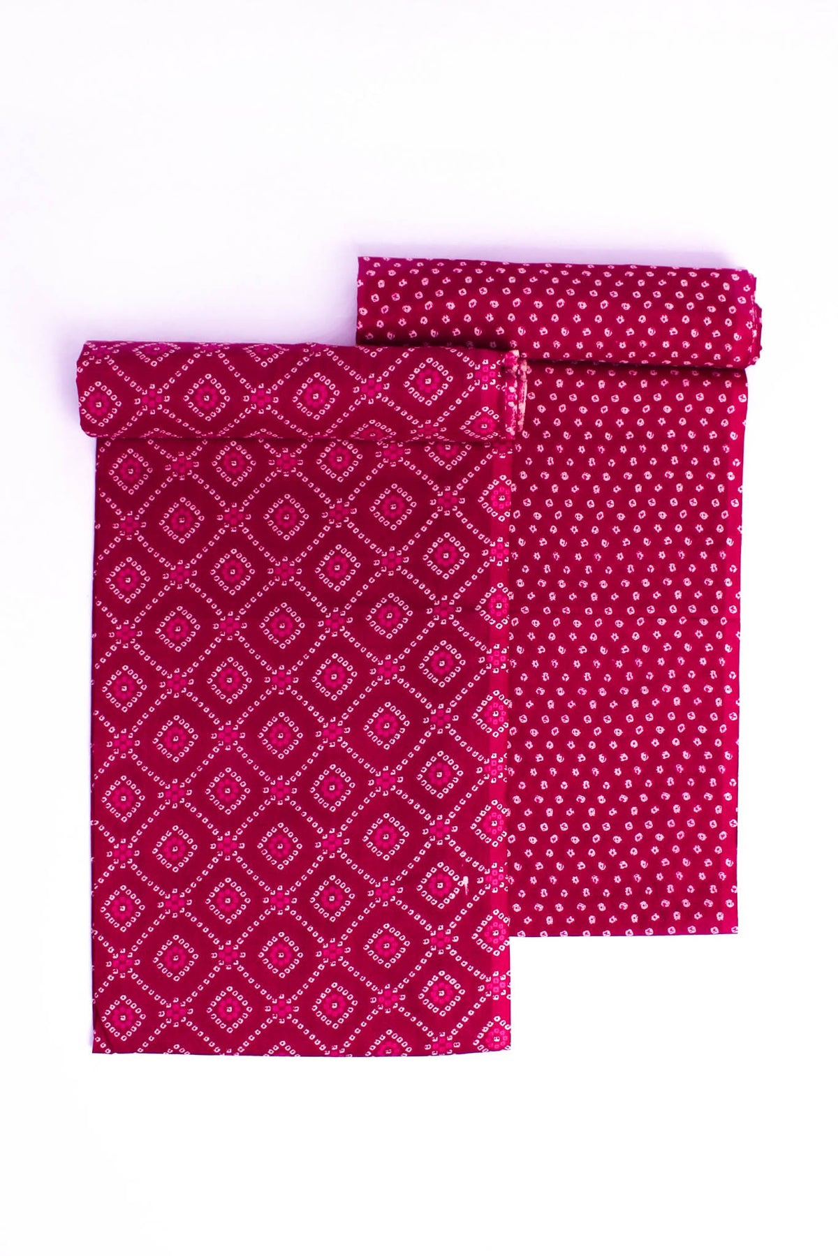 Two folded pieces of fabric with Bandhej-inspired patterns, one in pink and the other in a darker shade, possibly red, laid flat on a white background.