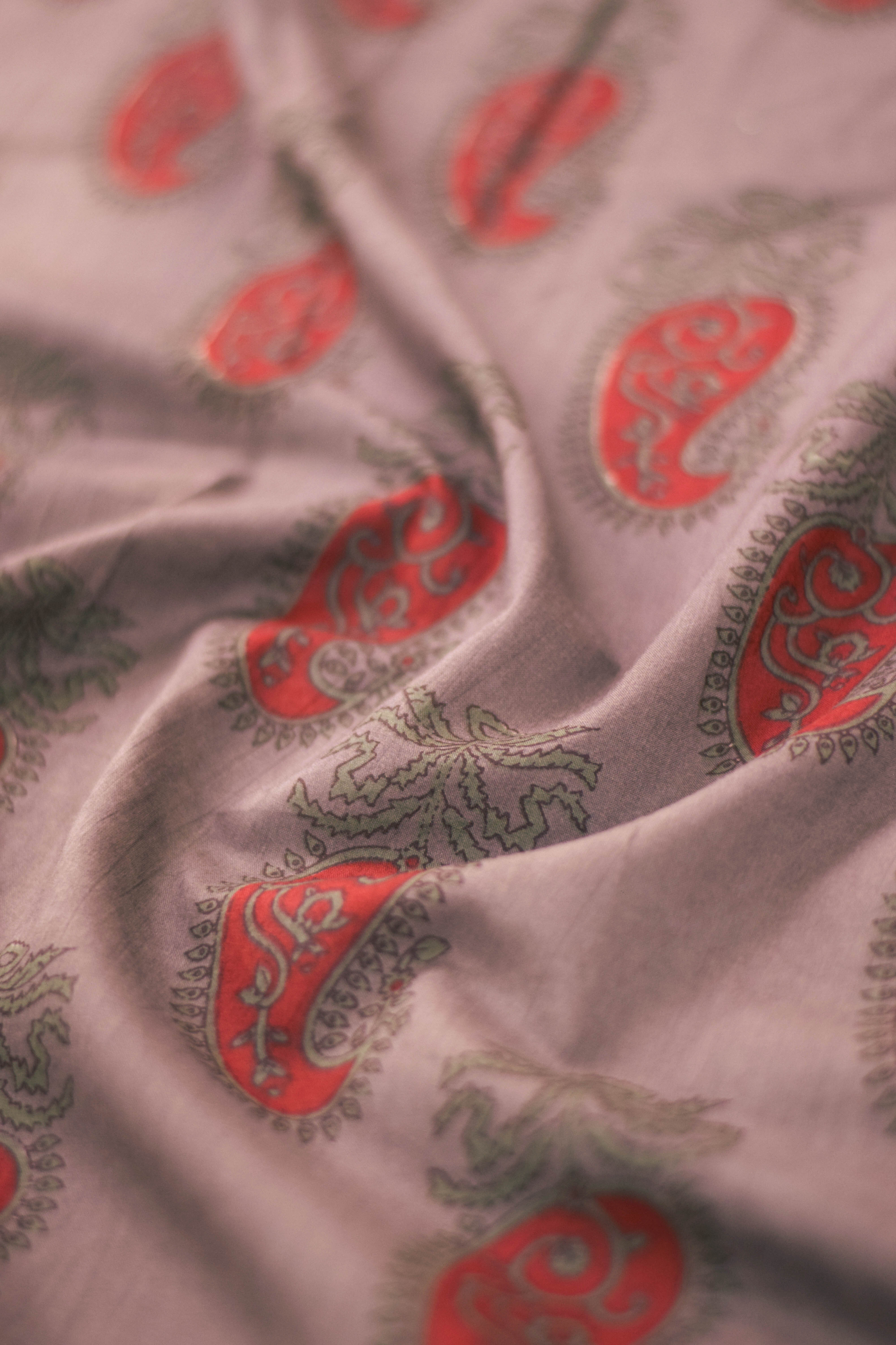 Close-up of paisley patterned fabric in red and green on a light background.