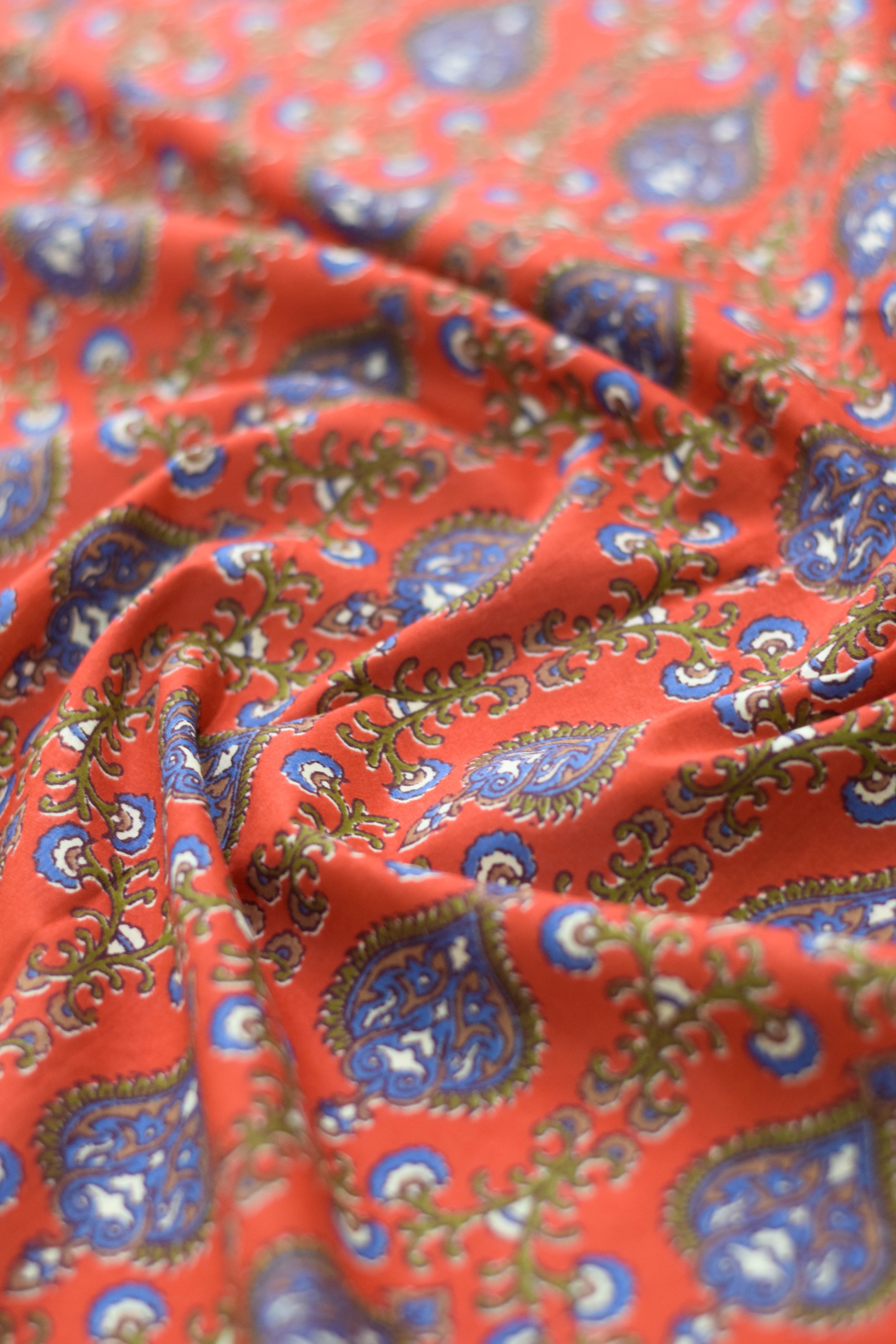 Close-up of red fabric with blue and green paisley patterns.