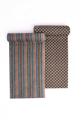 Two pieces of fabric, one with horizontal rust and blue stripes and another with a brown geometric buti pattern, likely representing a suit set and a dupatta.